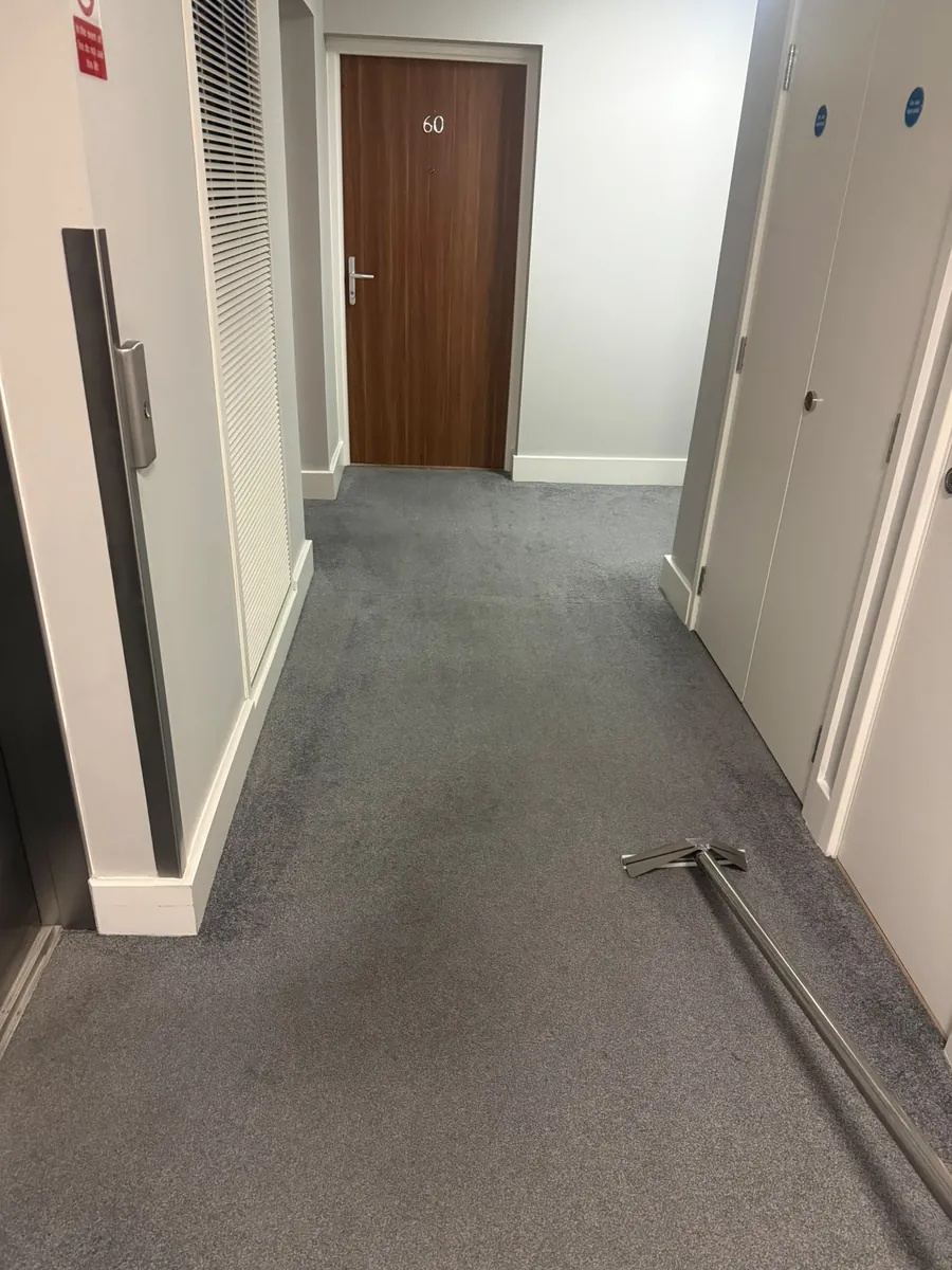 The same communal corridor after hot water extraction, spotting removed, wand resting on the cleaned carpet